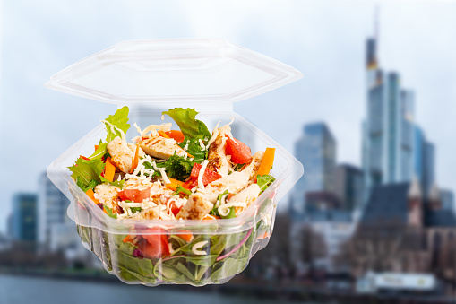 Plastic container that is used to sell large salads to go with a large city landscape in the background