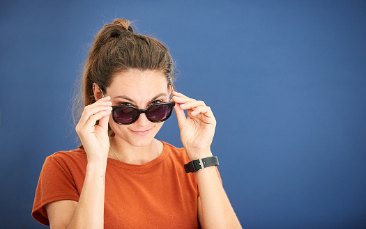 Portrait of a stylish young woman wearing sunglasses and looking at camera against blue background