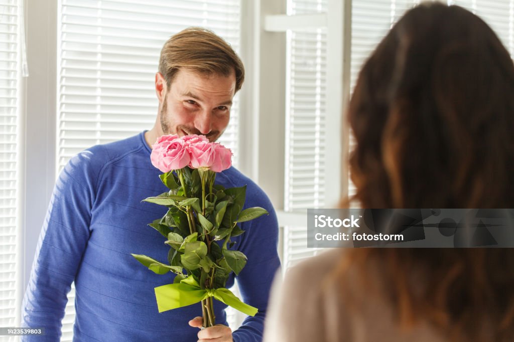 Man smelling the roses he is about to give to his loving wife Selective focus shot of romantic mid adult man smiling and smelling the roses he is about to give to his loving wife. Men Stock Photo