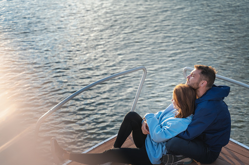 Young romantic couple sitting on the bow of a yacht during sunset. River travel and honeymoon concept