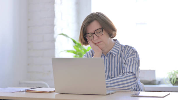 istock Senior Woman Sleeping While Sitting in Office with Laptop 1423541028