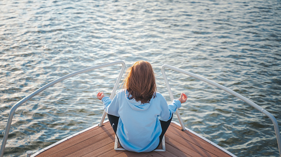 Young woman relaxing and meditating while sitting in a lotus position on the prow of a boat on the water