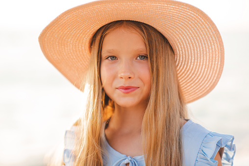 Smiling blonde teenage girl 12-14 year old wear straw hat over sun light outdoor. Look at camera. Summer season. Childhood.
