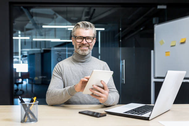 istock Portrait of successful programmer team leader, mature gray-haired engineer testing new app on tablet computer, businessman working inside modern office building, smiling and looking at camera. 1423544122