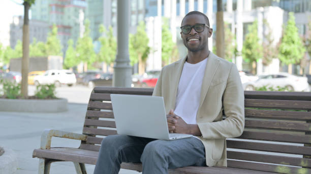 istock Agree African Man in Acceptance While using Laptop Sitting Outdoor on Bench 1423548842