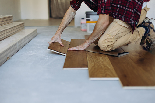 The man is installing the wooden plank of the parquet floor in his home during home improvement