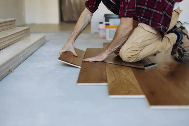 The man is installing the wooden plank of the parquet floor in his home during home improvement