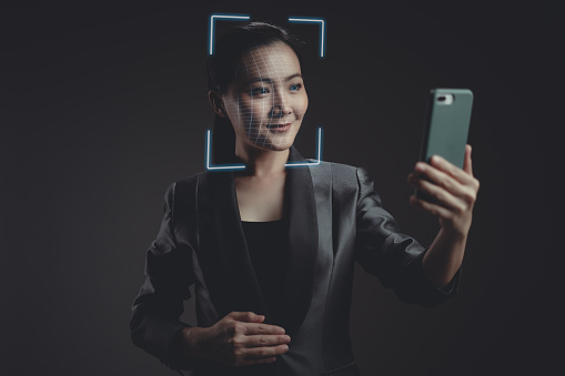 Asian woman scans face by smart phone using facial recognition system. Isolated on background.