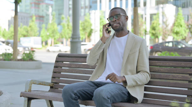 istock African Man Talking on Phone while Sitting Outdoor on Bench 1423551031