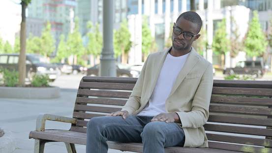 Tired African American Man Sleeping while Sitting Outdoor on Bench