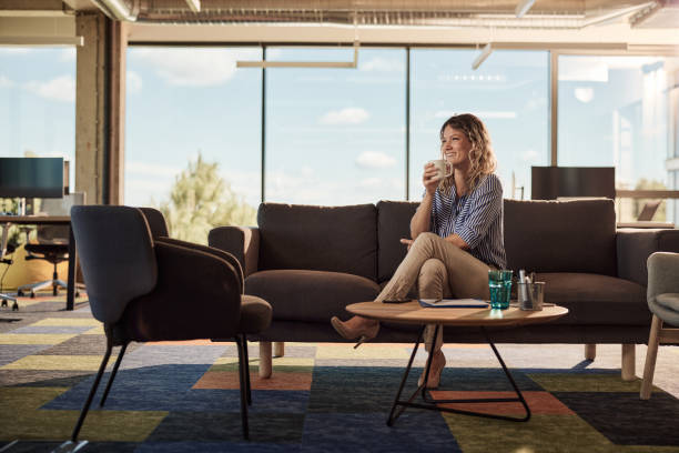 istock Happy businesswoman drinking coffee on sofa in modern office. 1423553059