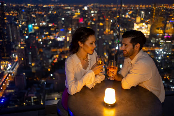 caucasian couple celebrating holiday event at luxury rooftop bar at night. - dating restaurant dinner couple imagens e fotografias de stock