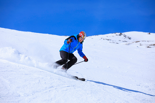 Vital senior,  men snow skier skiing, enjoying on sunny ski resorts. Skiing carving at high speed against blue sky.