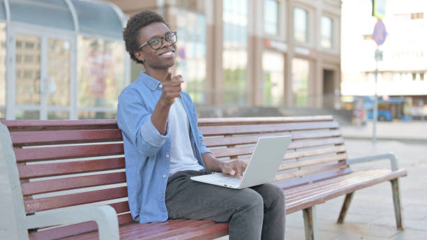 istock Young African Man Pointing at the Camera while Sitting on Bench Outdoor 1423557342