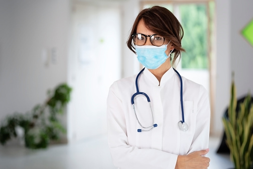 Confident female doctor standing at hospital corner and wearing face mask for prevention.