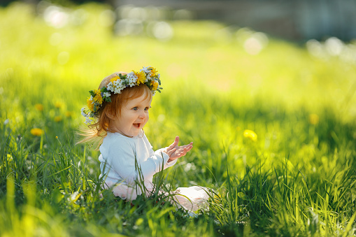 Cute little girl is wearing beautiful spring wreath outdoors, space for text. Red hair baby is spending time on nature