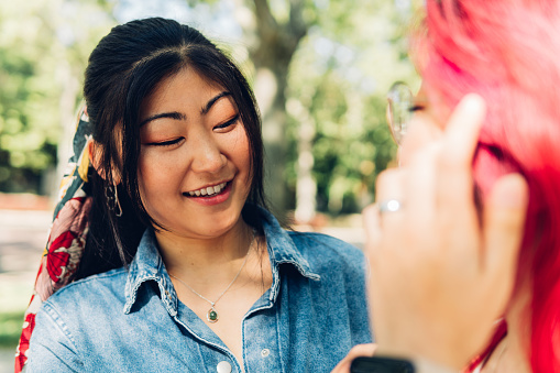 Positive young Asian woman with dyed hair smiling talking to her friend in the park on a sunny day