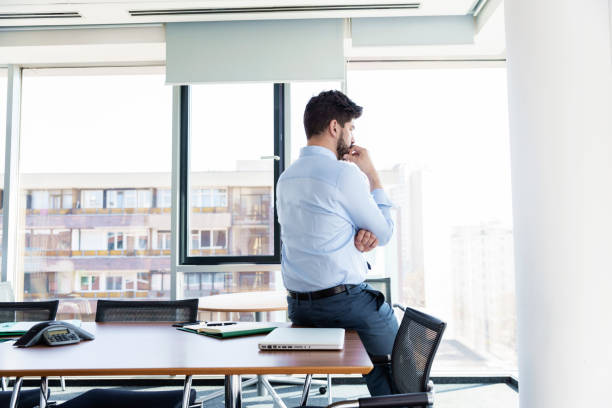 istock Thinking businessman looking out the window while standing at the office 1423561190
