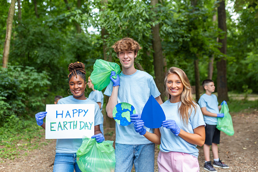 Diverse Group of People Picking Up Trash in The Park Volunteer Community Service. Happy international volunteers holding placard with 'happy Earth day' message.