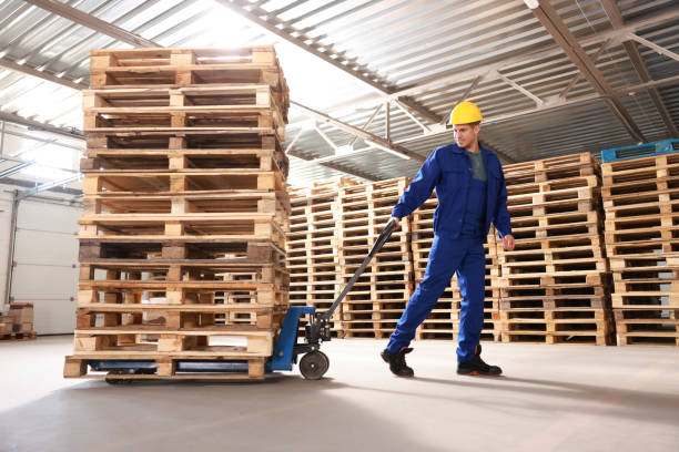 Worker moving wooden pallets with manual forklift in warehouse Worker moving wooden pallets with manual forklift in warehouse palette stock pictures, royalty-free photos & images