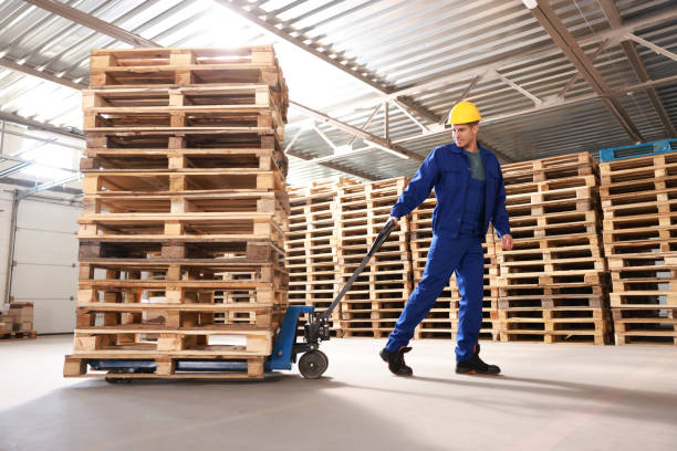 worker moving wooden pallets with manual forklift in warehouse - palete imagens e fotografias de stock