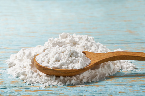 Close-up of cornstarch or flour powder in wooden spoon with wooden table.