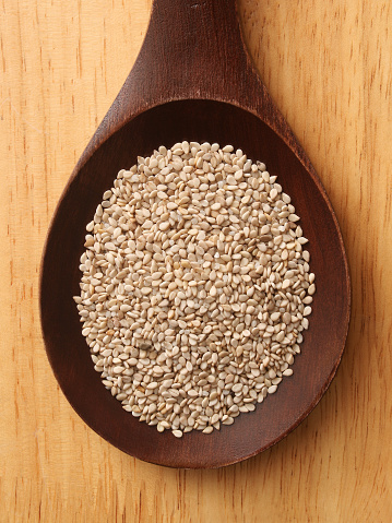 Top view of wooden spoon over table with wholegrain sesame seeds on it