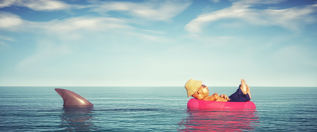 Hombre relajándose en una bobina de natación en el océano y un tiburón detrás de él. Concepto descuidado y relajado. photo