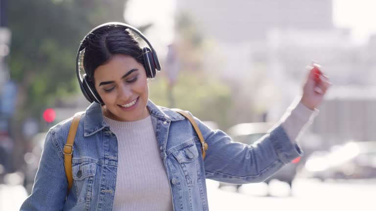 Music, headphones and dance of a happy woman in the city singing and dancing in urban freedom. Positive female in joyful life happiness with smile singing for wireless audio moving to sound in a town