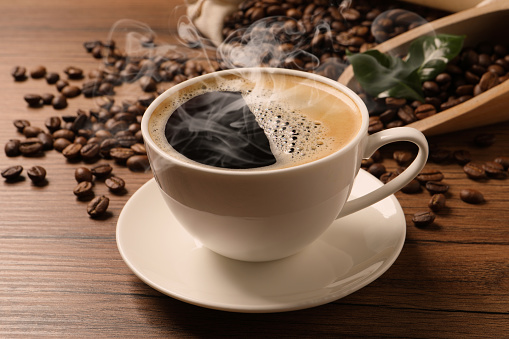 Cup of aromatic hot coffee and beans on wooden table, closeup