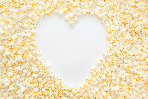 Popped popcorn kernels filling the frame with negative space showing a heart in white.