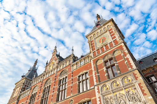 Amsterdam Central station building exterior front seen from the station square (Stationsplein) with a blue sky and fluffy clouds in the background.