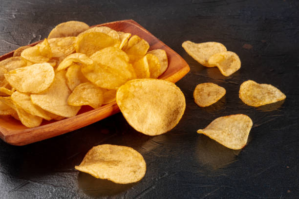 istock Potato chips or crisps in a bowl and scattered on a black stone background 1423575622