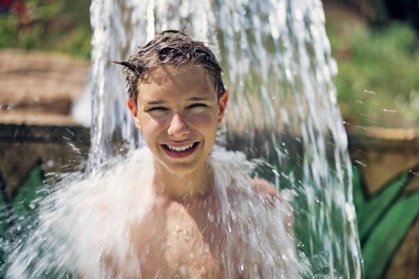 ragazzo adolescente che si diverte a essere spruzzato nel parco acquatico - splashing color image front view head and shoulders foto e immagini stock