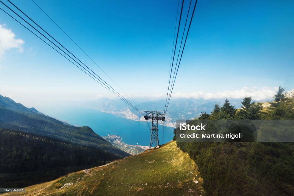 Cable car wires and glimpse of Lake Garda seen from Monte Baldo, Italy Cable car wires and glimpse of Lake Garda seen from Monte Baldo. Monte Baldo (German: Waldberg) is a mountain range in the Italian Alps, located in the provinces of Trento and Verona; the ridge is reachable through a cable car from the nearby town of Malcesine, on the shore of Lake Garda. Beauty Stock Photo