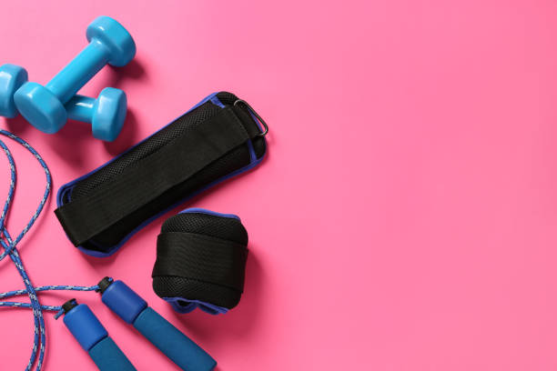 istock Blue ankle weights, dumbbells and skipping rope on pink background, flat lay. Space for text 1423576524