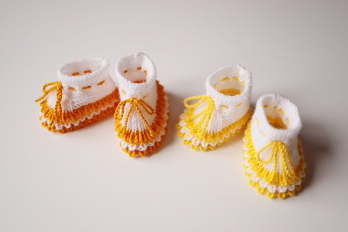 Two hand-knitted woolen orange and yellow striped white baby booties on a white background
