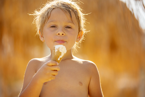 Happy child, boy eating ice cream  on the beach, enjoying summer, playing. Halkidiki, Greece