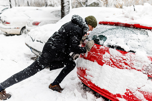 Photo of a Man Pushing Broken and Frozen Car, Stuck in the Snow. Winter, People, and Car Problem Concept.