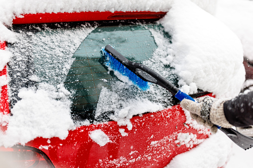Man is Cleaning Snow from a Car with a Brush. Man Outdoors is Cleaning Snow on his Car Windshield.