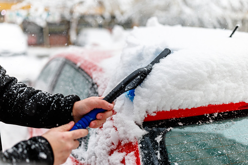 A Man in the Street is Cleaning Snow from a Car Covered with Heavy Snow.