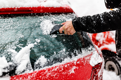 A Man has Snow Problems with a Car so he is Cleaning Ice from a Windshield.
