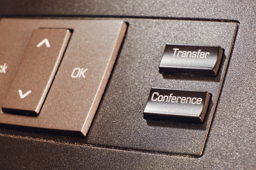 A button with the text transfer and conference on a landline phone in the office, close-up