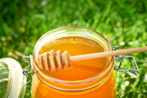 istock Open jar of  honey  on the grass, sunlight. Top view. 1423584014
