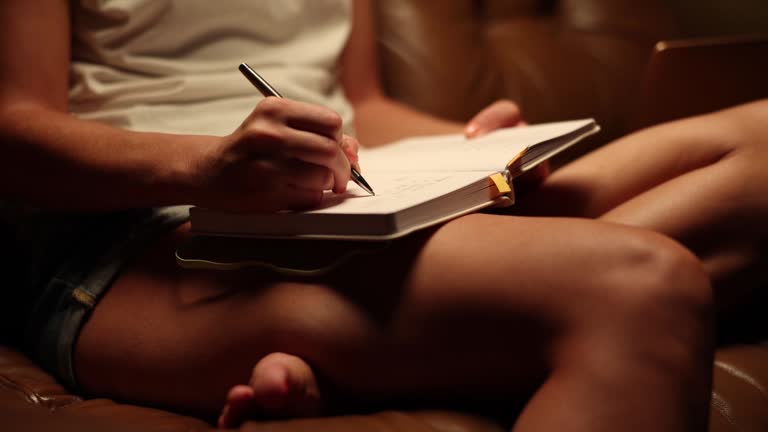 Woman writer writes in journal notebook or diary with pen and sits on sofa