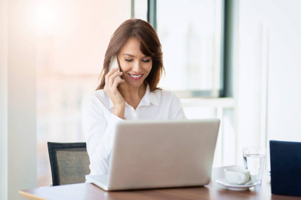 istock Confident businesswoman using mobile phone and laptop while working at the office 1423589404