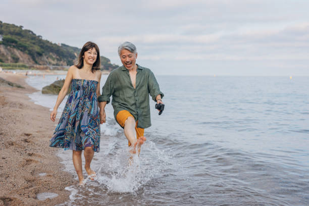 happy attractive couple walking on beautiful sunny beach - couple walking old middle imagens e fotografias de stock