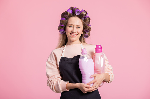 A smiling housewife prepares to do laundry at home. The woman holds in hands a floral fabric softener with a pleasant fragrance choosing the right liquid.