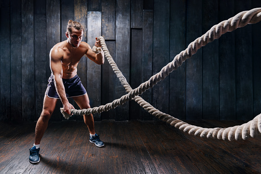 Dynamic motion of sportive muscular man, athlete do exercise fitness with battle ropes. Male training upper body working out at hard gym training. Brutal strong bodybuilder pumping up muscles.