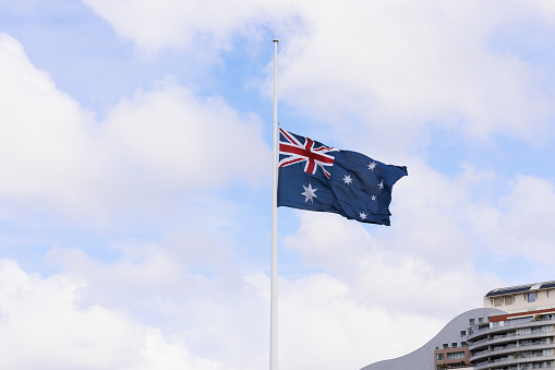 Australian flag at half mast against a cloudy sky.